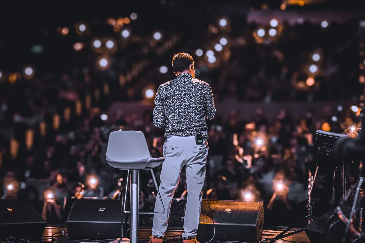 A speaker on stage before an audience holding up phone lights