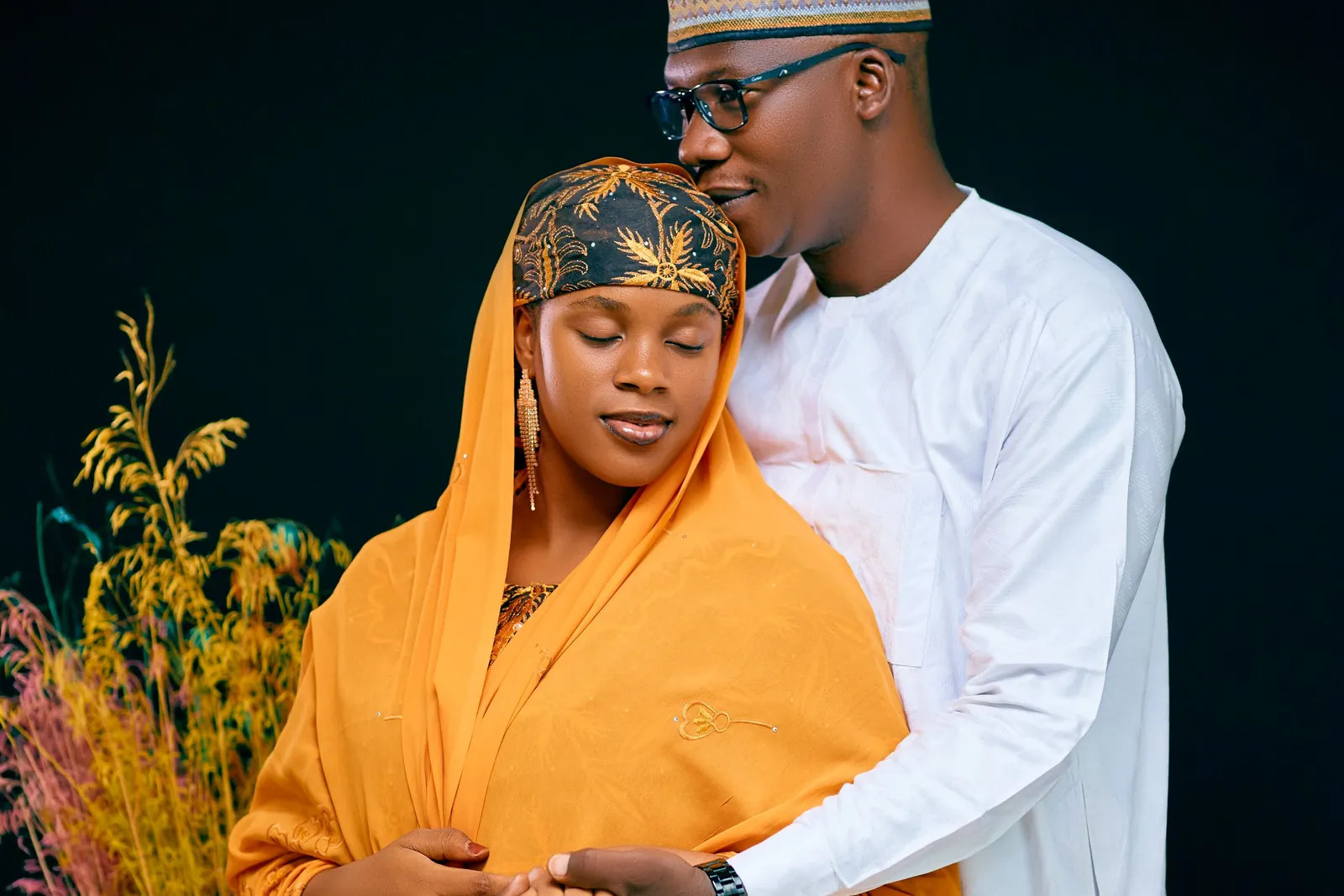A couple in orange and white traditional attire, photographed against deep green at their engagement