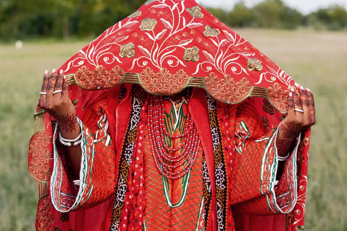 A bride in layered red beads and veil at a traditional engagement